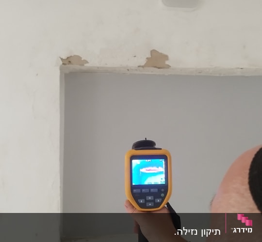 אדם מחזיק מכשיר תרמי מול קיר עם קילופים